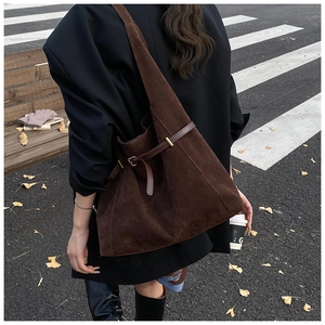 Close-up of deep brown suede tote bag featuring smooth leather straps and gold buckles