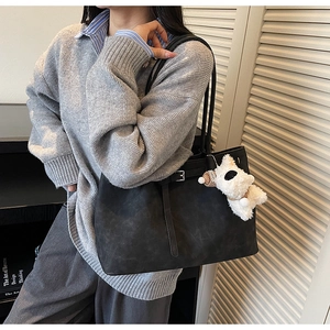 Detail of black matte tote bag with silver buckle strap and cute white puppy plush charm