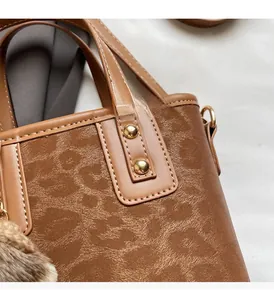 Détail du sac seau marron à texture léopard avec clous dorés et pompon en peluche
