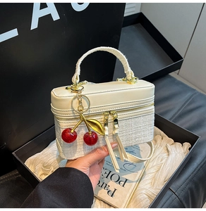 Detail of white tweed and leather handbag featuring cherry charm and dual zipper