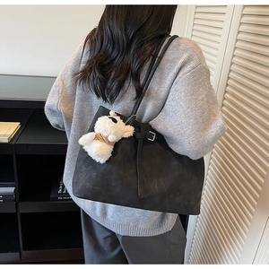 Detail of black suede tote bag with buckle strap and a white alpaca plush charm