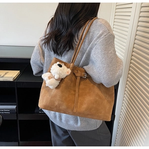 Detail of large brown suede tote bag with side buckle and plush bear charm on model