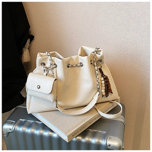 Detail of cream tote bag with drawstring, silver chain strap, and wood bead charm