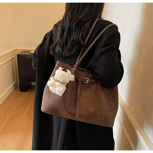 Detail of a dark brown suede tote bag with slim straps and a white plush charm