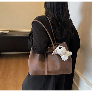 Close-up of a large brown suede tote bag with a cute white plush puppy charm on the handle