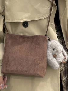 Brown frosted suede bucket bag with plush bunny keychain in a stylish autumn outfit