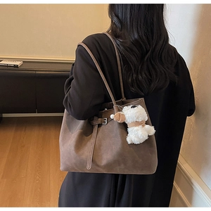 Detail view of large dark brown suede tote bag with plush puppy charm on a model's shoulder