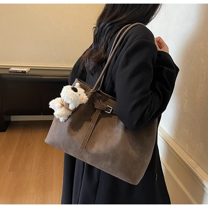 Detail of dark brown suede tote bag with strap buckle and white puppy plush charm