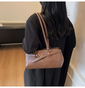 Detail of a brown leather shoulder bag with a gold metal buckle and ZHONMA logo
