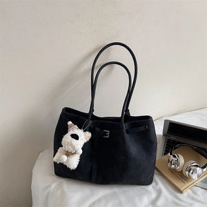 Detail of black suede tote bag with long handles and a cute white puppy plush charm