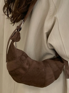 Deep brown matte leather croissant bag with wide shoulder strap worn on a beige coat