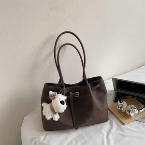 Close-up of brown matte tote bag with laptop, headphones, and a white plush dog pendant