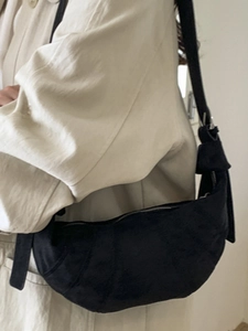Fashionable black crescent shoulder bag with knot strap detail worn with beige coat