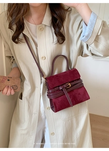 Chic burgundy suede handbag with gold buckle shown with a beige trench coat on a model