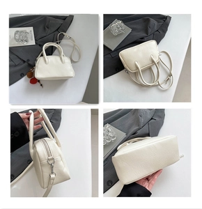 Detail view of cream Boston bag showing dual handles and beaded pompom charm accent