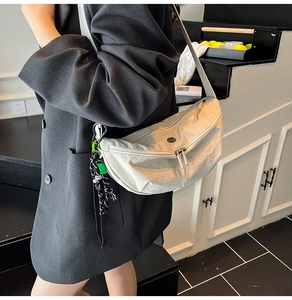 Detail van een beige nylon crossbody tas in halve maan vorm met dubbele rits en hanger