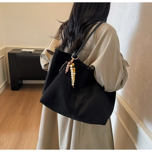 Detailed back view of a large black tote bag with beaded charm and khaki trench coat