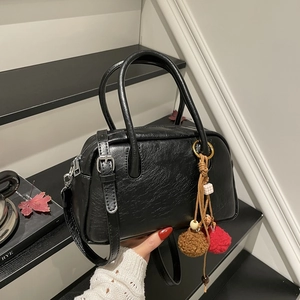 Detail of black Boston bag with textured leather, metallic ring, and plush pompom charm