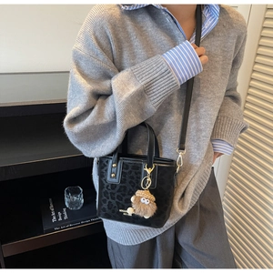 Détail d'un sac seau noir à gaufrage léopard avec un pendentif en peluche mignon