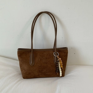 Detail view of large brown suede tote bag featuring artistic beaded strap ornament and handles