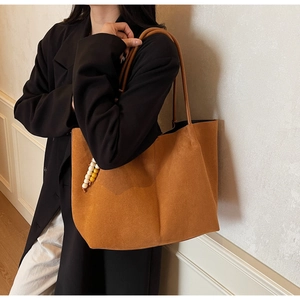 Detail of a brown suede tote bag with delicate vertical seams and a beaded charm on a model