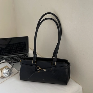 Detail of black faux leather shoulder bag with gold clasp next to a laptop and magazine