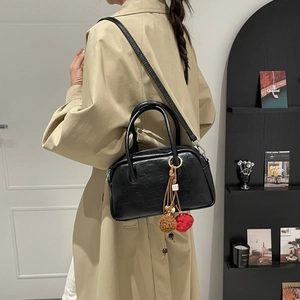 Detail view of a black retro Boston bag with textured leather and plush charm on a model