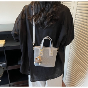 Détail d'un sac seau gris vintage avec breloque en peluche porté par un mannequin en intérieur