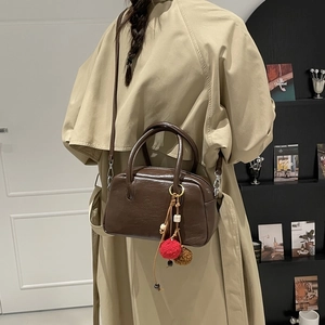 Detail of dark brown glossy leather Boston bag with creative multi-material charm and dual handles