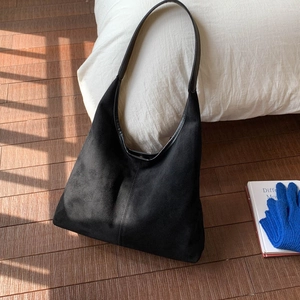 Detailed view of a black suede tote bag with slim straps on a sunlit wooden floor