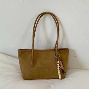 Detail of a brown suede tote bag featuring a decorative ethnic bead tassel on the shoulder strap