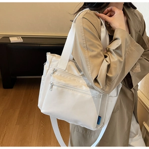 Close-up of white canvas tote bag featuring multiple zipper pockets and wide shoulder strap