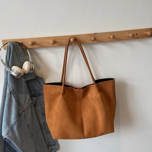 Brown suede tote bag with long leather straps hanging on a wooden hook in a lifestyle setting