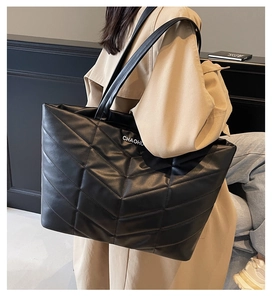 Detail of black quilted tote bag with V-shaped stitching and silver metal logo on shoulder