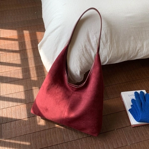 Detailed texture of dark burgundy suede tote bag with slim leather strap on wooden floor