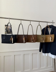 Detailed row of matte suede tote bags in five colors with decorative wooden bead tassels