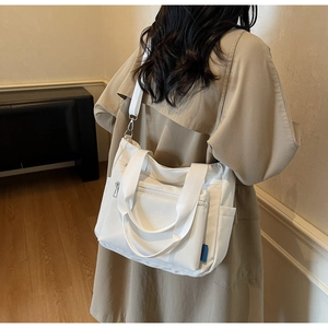 Rear view of model wearing white nylon tote bag with multiple pockets and wide shoulder strap