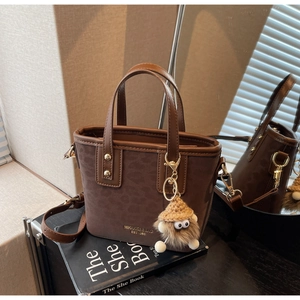 Détail du sac seau marron foncé avec imprimé léopard, lettrage doré et charme en peluche