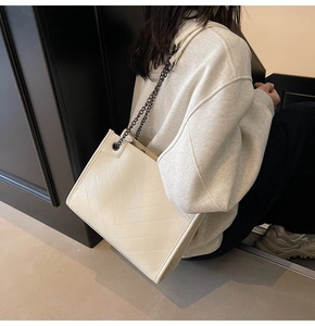 Vista laterale della borsa tote trapuntata beige con catena nera indossata da modella