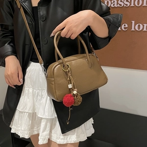 Close-up of brown Boston bag with red pompom charm and vintage matte leather detail