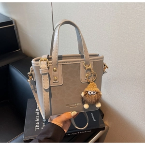 Détail du sac seau gris avec ferrures dorées et charmant monstre en peluche sur le côté