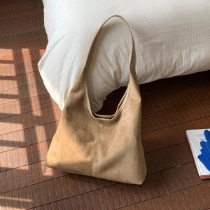 Detail shot of a large brown suede tote bag on a bed with natural sunlight and striped shadows