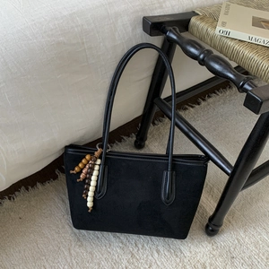 Detail view of black suede tote bag with decorative multi-color wooden bead charm