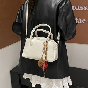 Detail of white Boston bag with natural texture, dual handles and colorful pompom charms