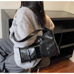 Close-up of black glossy leather shoulder bag featuring dual pockets and silver buckles