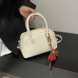 Detail of off-white leather Boston bag featuring colorful plush pom-pom charms and hardware