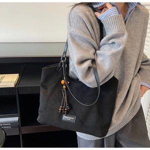Détail du sac cabas en daim noir avec bandoulière en cuir et pompons de perles