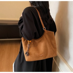 Détail du sac cabas en daim marron avec pendentif en perles et élégant logo métallique