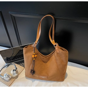 Détail du sac cabas en daim marron avec pompon décoratif dans un cadre de bureau
