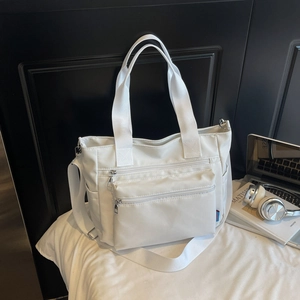 Detailed view of white nylon tote bag showing multiple zipper pockets and wide straps